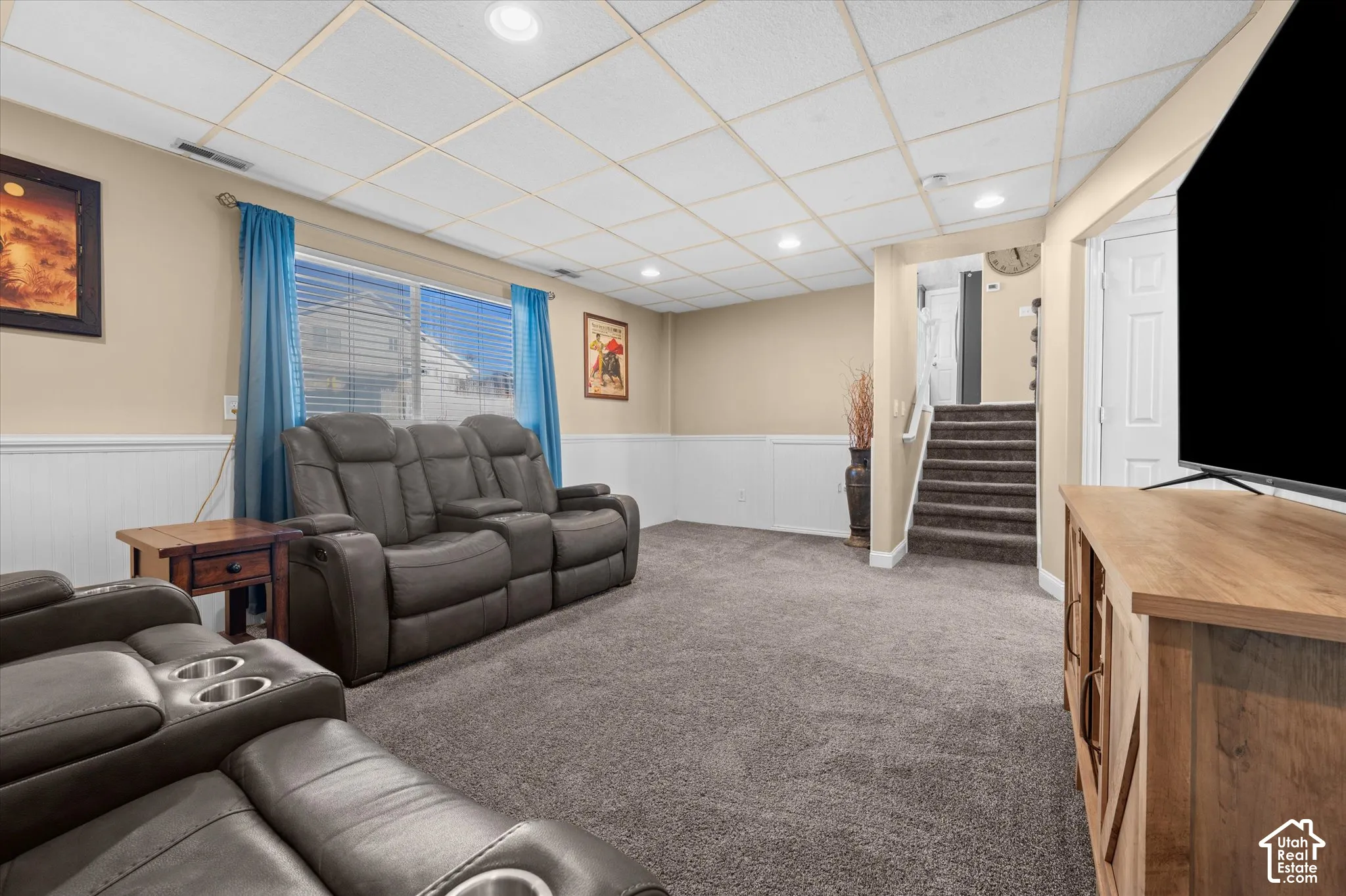 Carpeted lower-level room featuring recessed lighting, a drop ceiling, two-tone painted walls with wainscoting, and a window with blinds
