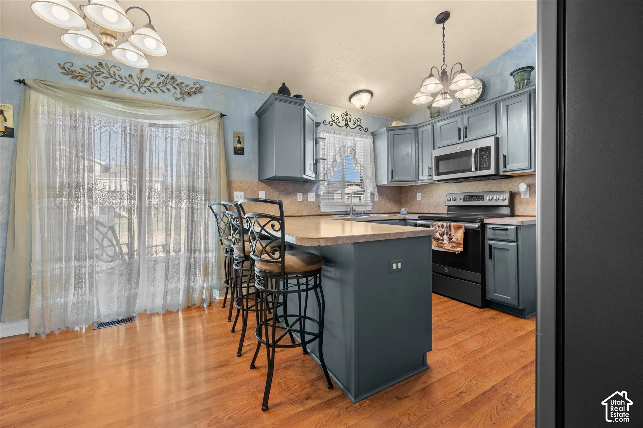 Spacious kitchen featuring an island with counter seating, wood-finish flooring, full cabinetry, stainless steel microwave, and a range with a black finish