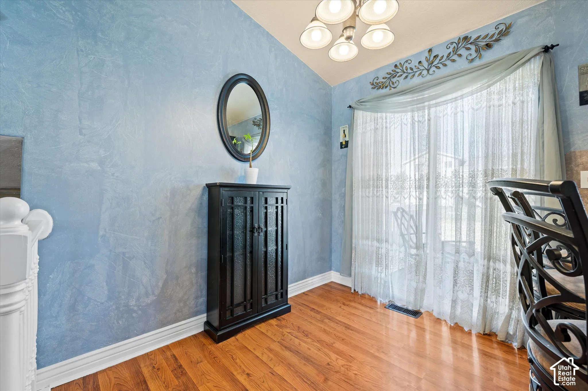 Interior space featuring hardwood flooring, a large window with sheer drapery, a textured wall finish, and a ceiling-mounted light fixture