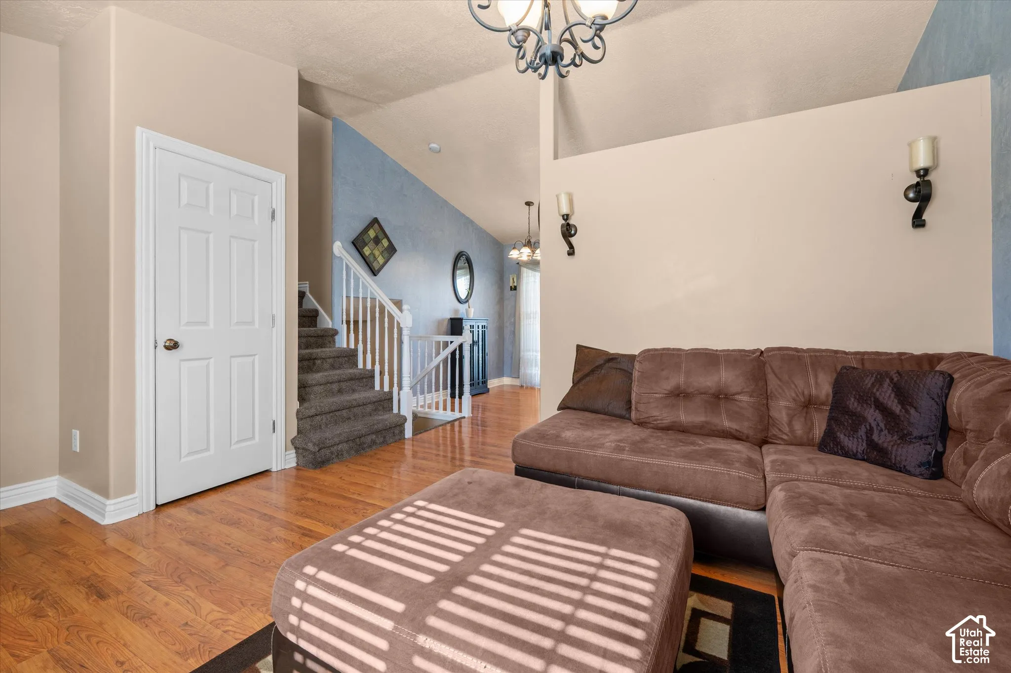 Spacious living area featuring wood-finish flooring, vaulted ceilings, and a carpeted staircase with white balusters