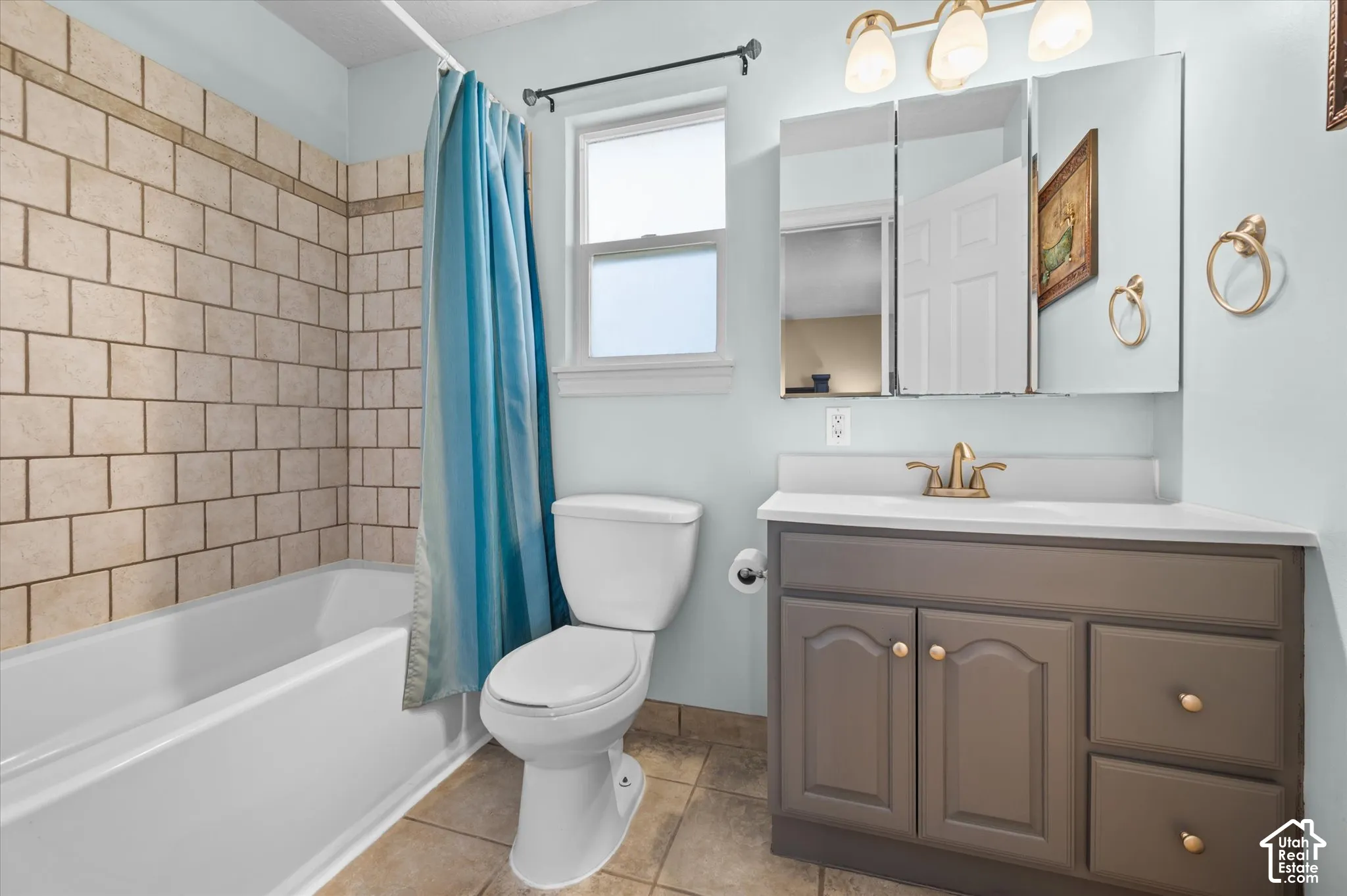 Bathroom featuring a white tub with light-toned subway tile surround, a single window, and a vanity with a white countertop and brass-finish fixtures