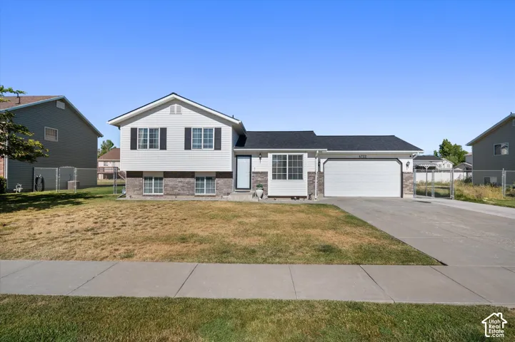 Split-level residence featuring a two-car garage with an asphalt driveway, white siding, and a stone facade accent