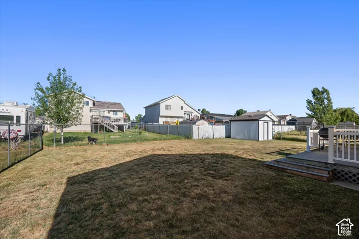 Expansive backyard featuring a chain-link fence perimeter, mature trees, a detached storage shed, and a raised wood deck