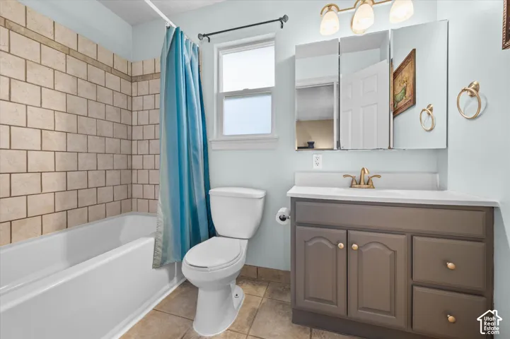 Bathroom featuring a white tub with light-toned subway tile surround, a single window, and a vanity with a white countertop and brass-finish fixtures