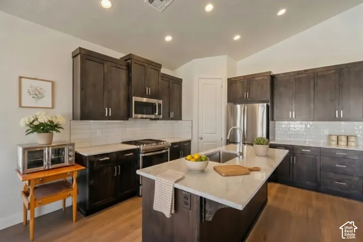 Kitchen featuring dark wood-finish cabinetry, stainless steel appliances, a large center island with an undermount sink, marble-look countertops, and recessed lighting Virtually Enhanced