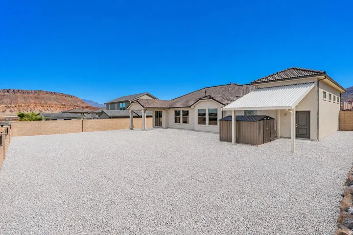 Extensive gravel backyard featuring a stucco exterior, covered patio, and a tiled roofline