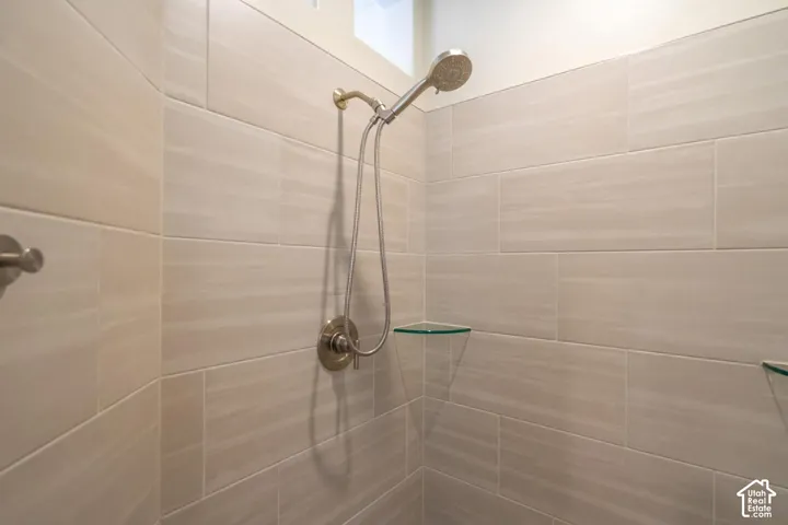 Shower featuring large format light-toned tile, brushed nickel fixtures, and built-in glass corner shelves