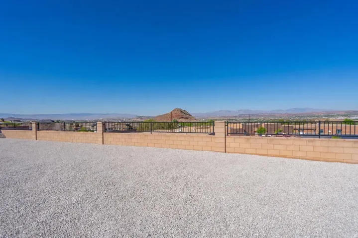Gravel ground cover bordered by a block wall with metal fencing, offering distant mountain scenery