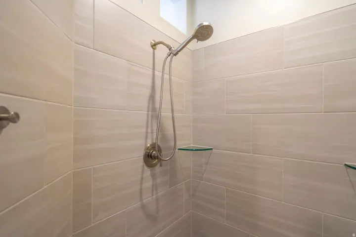 Shower featuring large format light-toned tile, brushed nickel fixtures, and built-in glass corner shelves