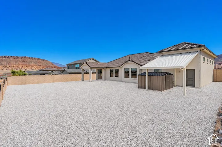 Extensive gravel backyard featuring a stucco exterior, covered patio, and a tiled roofline