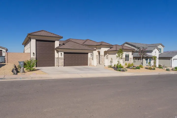 Contemporary stucco exterior featuring a multi-car garage, concrete driveway, and desert-style landscaping