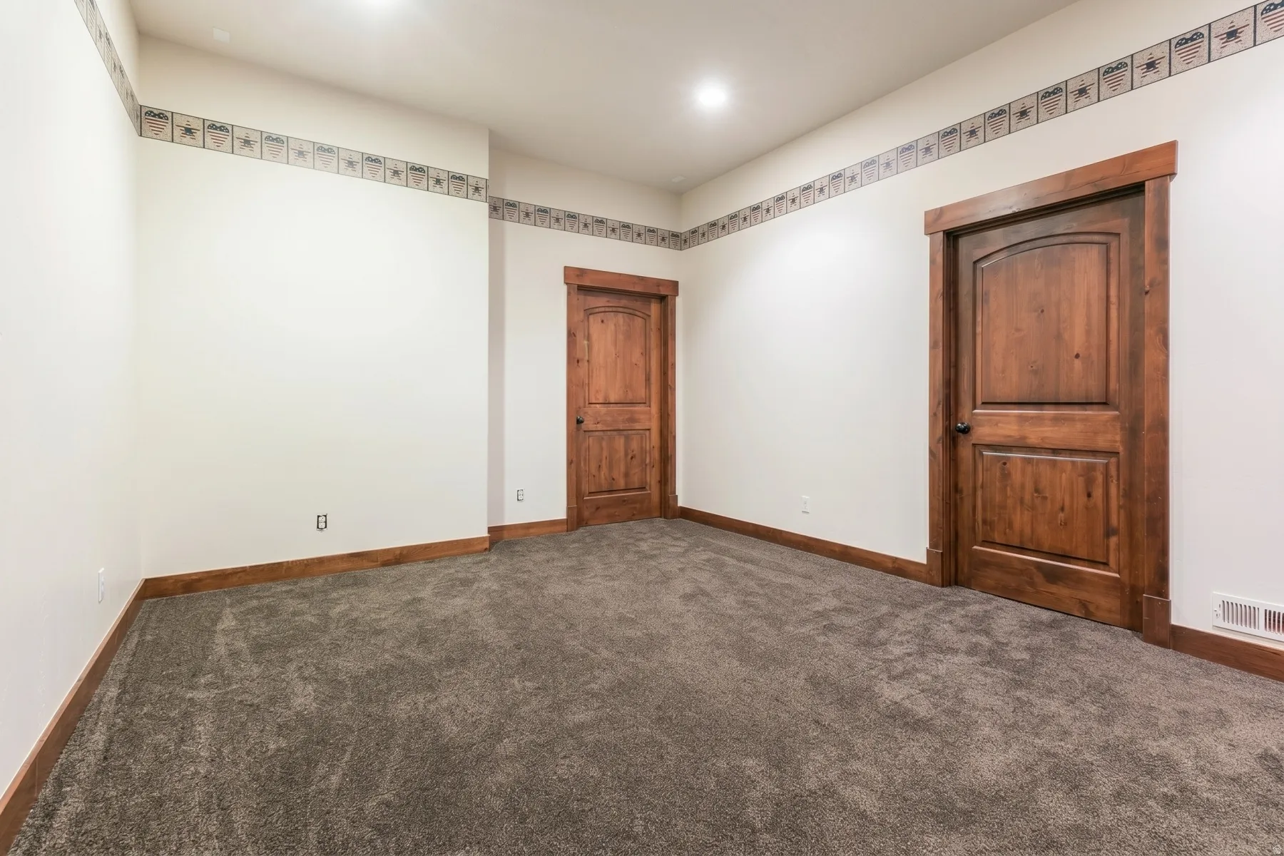 Carpeted room featuring two solid wood doors with arched top panels, wood trim, and a decorative border