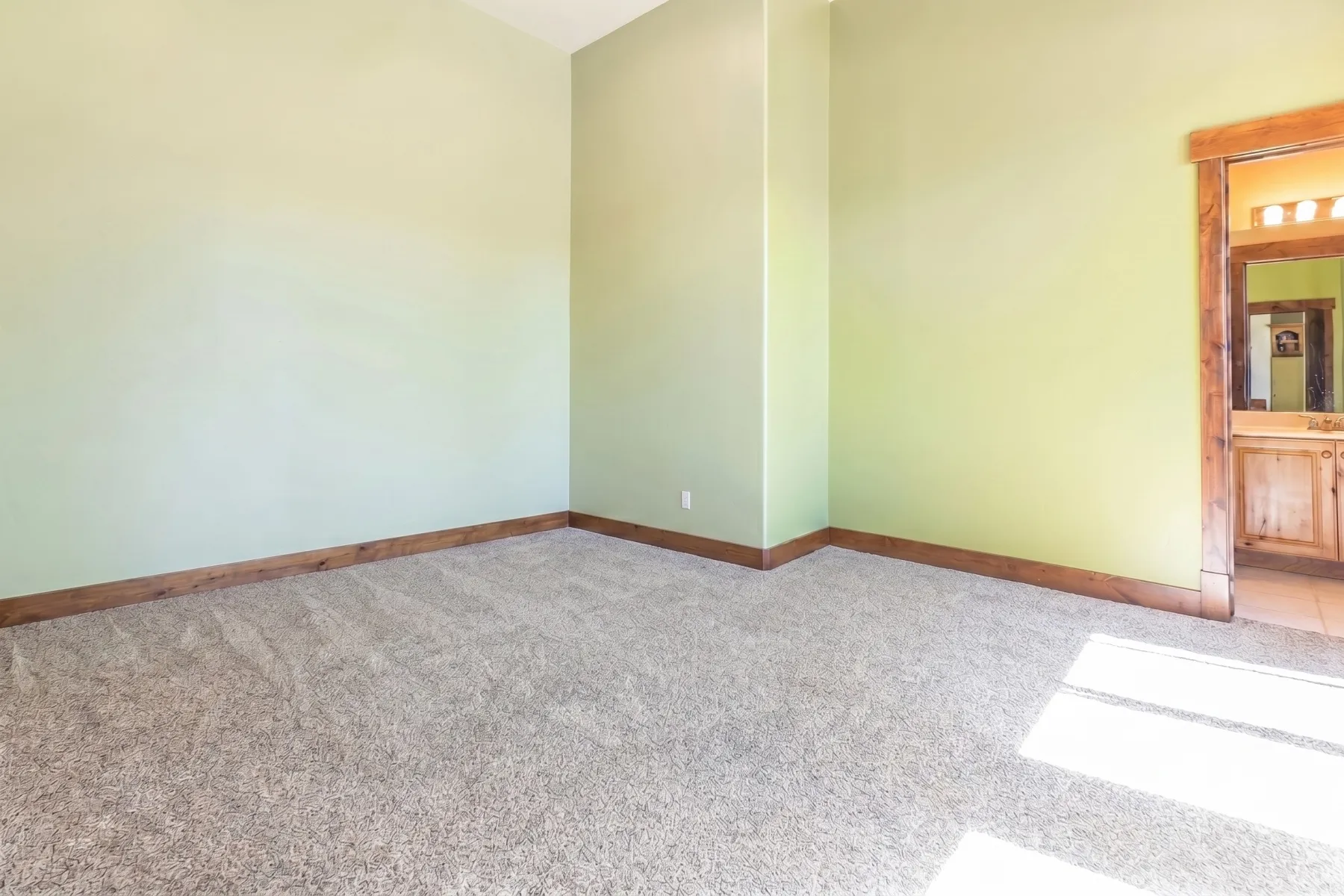 Carpeted room with light green walls and wood-finish baseboards