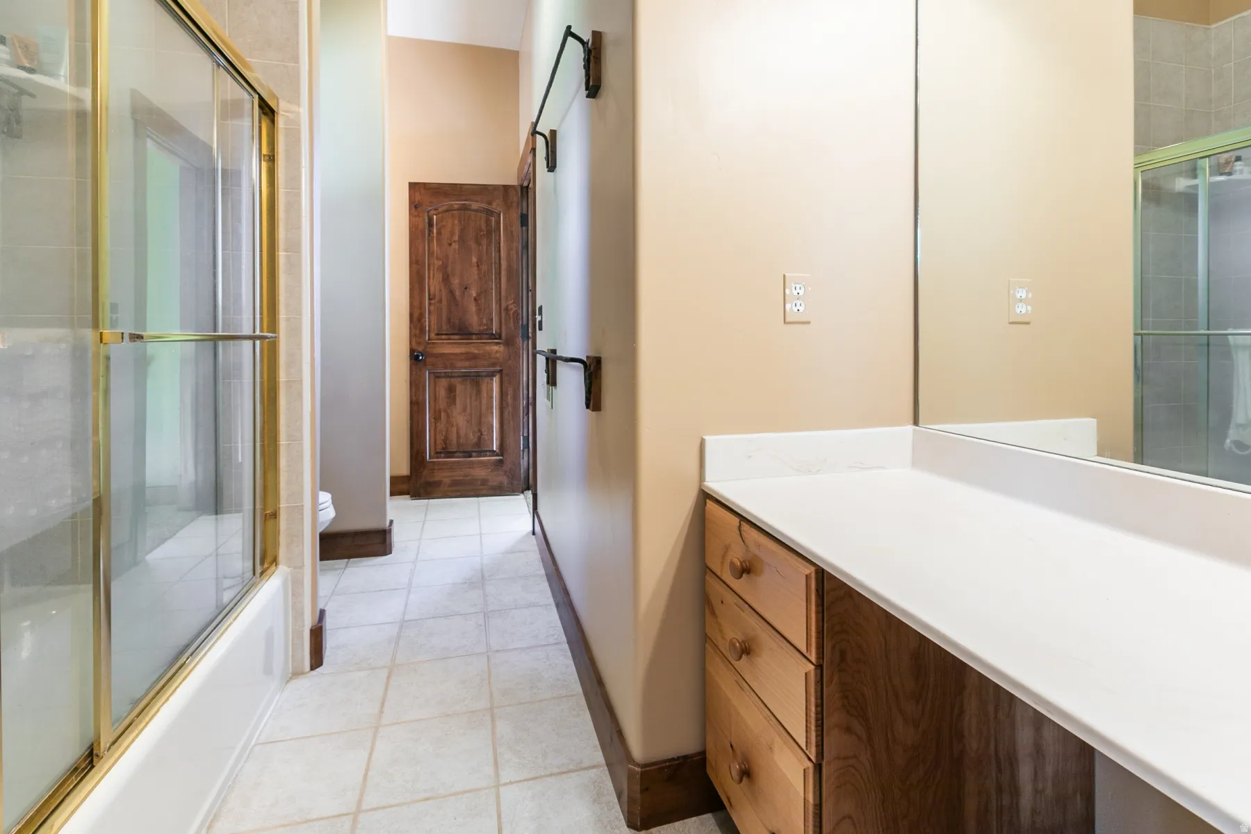 Bathroom featuring a vanity with a light wood-finish countertop, a large wall-mounted mirror, and a wood-paneled door