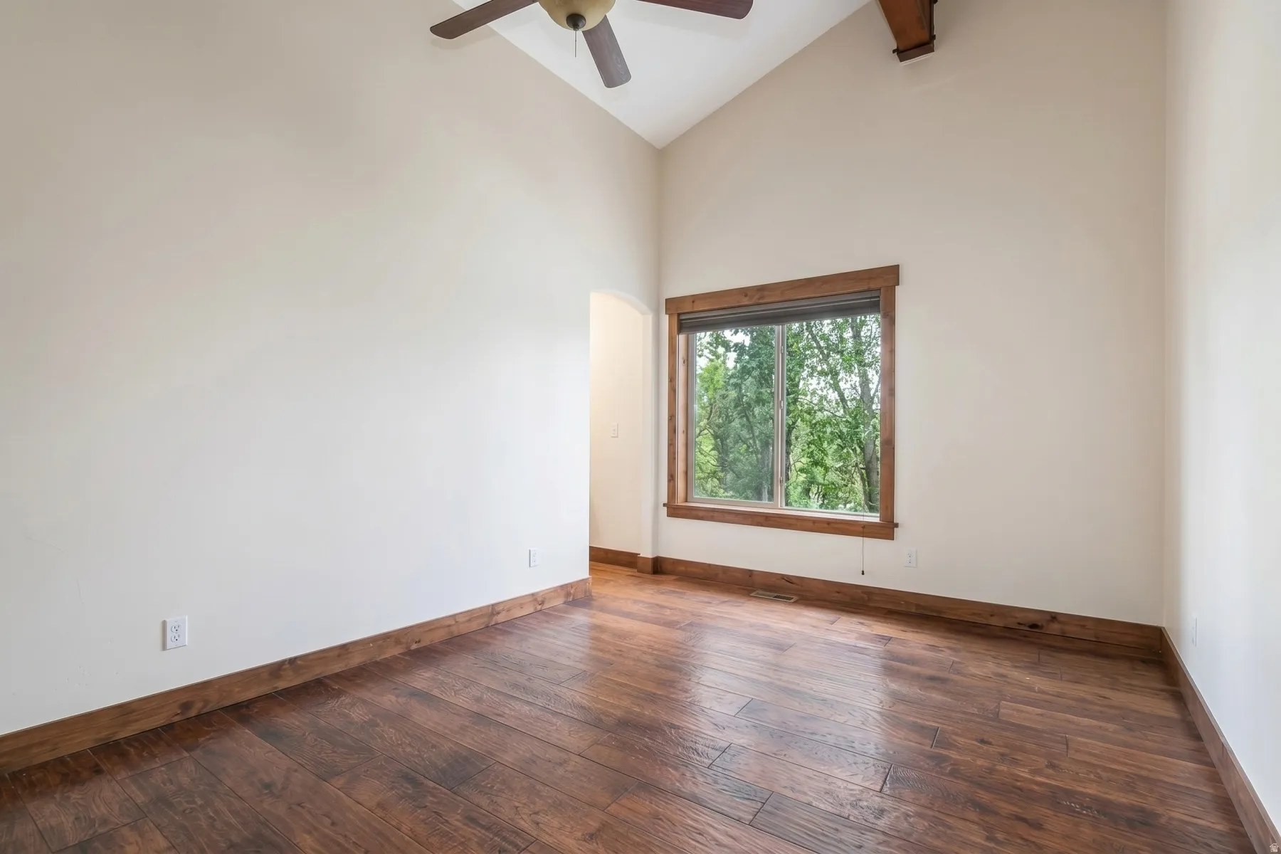 Vaulted ceiling with exposed wood beam and ceiling fan, wood-finish flooring, and a window with wood trim