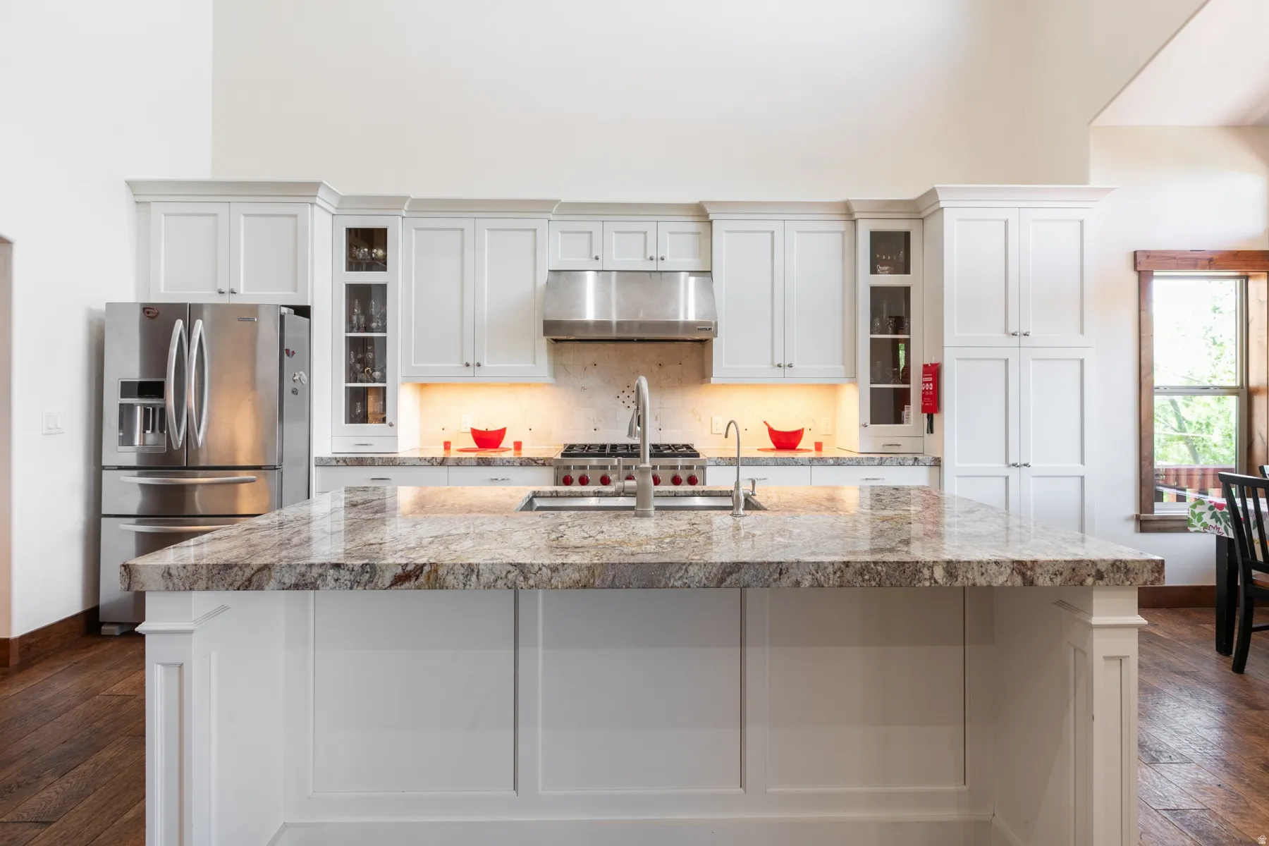 Kitchen island with a polished stone countertop, white paneled cabinetry, stainless steel appliances, and wood-finish flooring