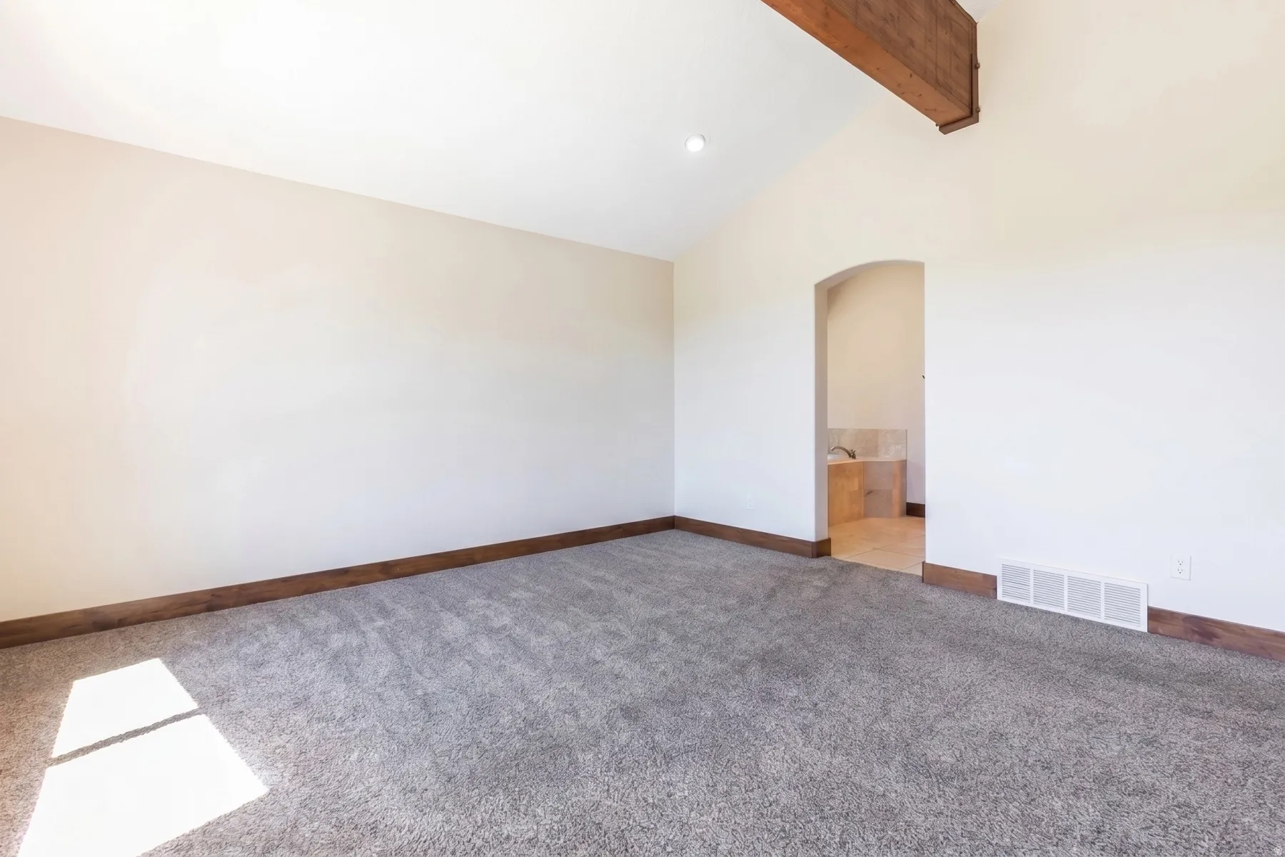 Vaulted ceiling featuring an exposed wood beam, neutral wall paint, and gray carpet