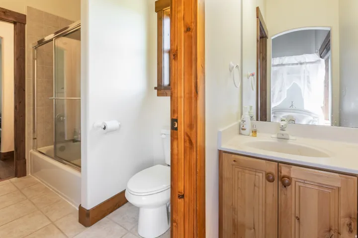Bathroom featuring light-toned tile flooring, a white vanity with wood-finish cabinetry, a white countertop, and a built-in sink with a chrome faucet