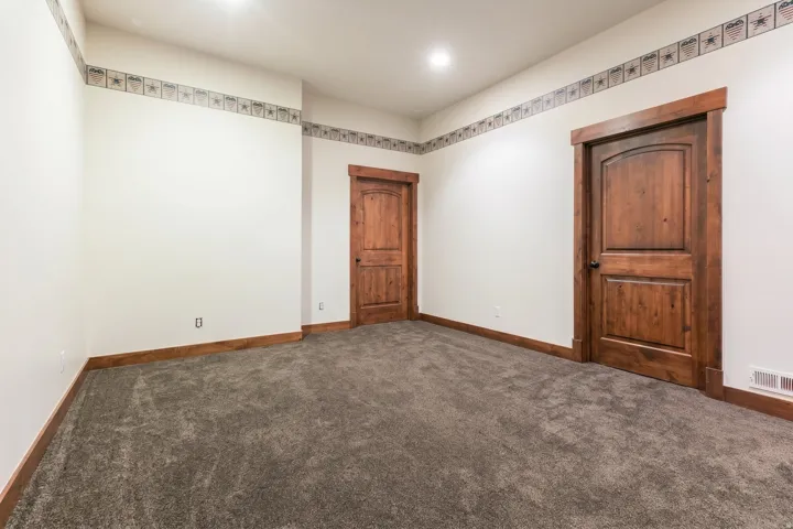 Carpeted room featuring two solid wood doors with arched top panels, wood trim, and a decorative border