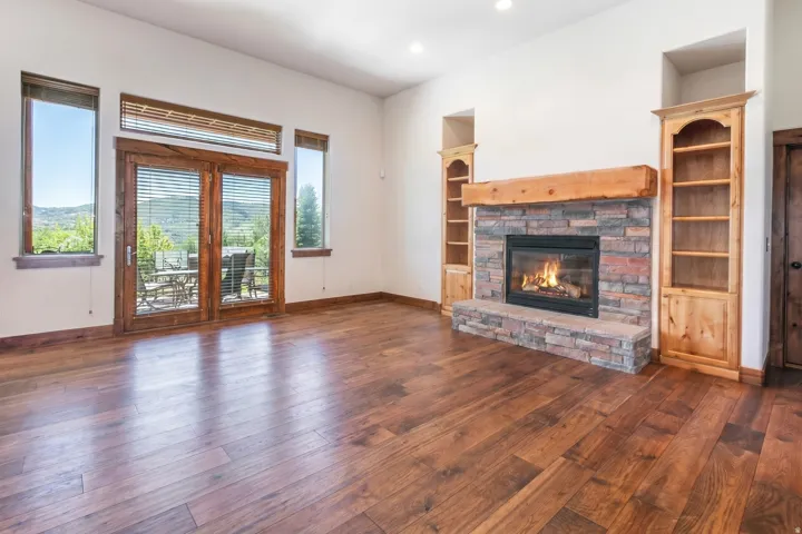 Spacious living area featuring rich wood-finish flooring, a stone-surround fireplace with a substantial timber mantel, and integrated built-in shelving