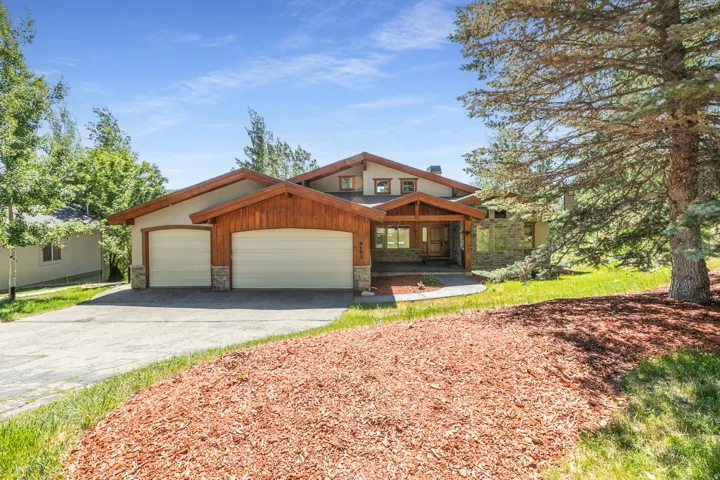 Expansive residence featuring a multi-gable roofline, stone and wood-paneled exterior accents, a two-car garage, and a covered entry porch