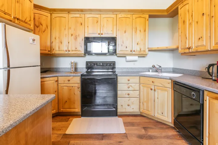 Full kitchen featuring light wood cabinetry, stone-finish countertops, black appliances, and wood-finish flooring
