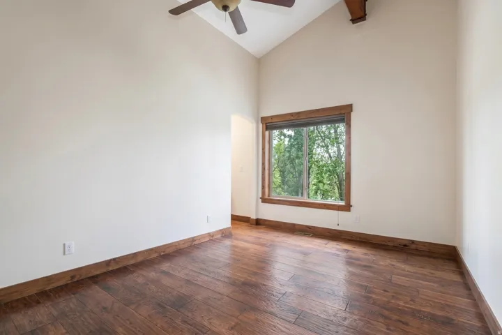 Vaulted ceiling with exposed wood beam and ceiling fan, wood-finish flooring, and a window with wood trim