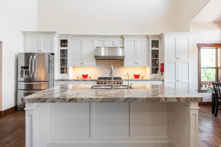 Kitchen island with a polished stone countertop, white paneled cabinetry, stainless steel appliances, and wood-finish flooring