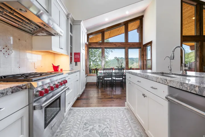 Gourmet kitchen featuring a stainless steel range with red accents, white cabinetry, polished countertops, and a tile backsplash
