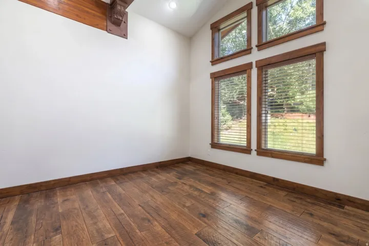 Vaulted ceiling room featuring natural wood-finish flooring, white walls, and a prominent wood beam with decorative corbel