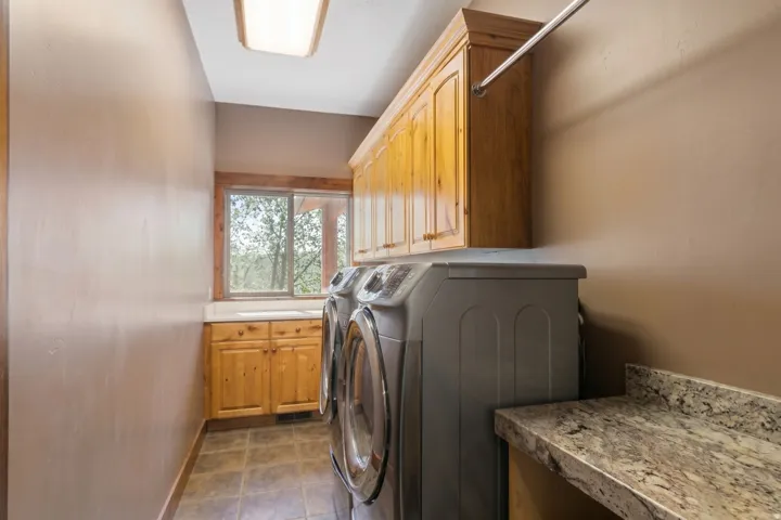 Laundry room featuring wood-finish cabinetry, a utility sink, a window with exterior scenery, a wall-mounted drying rod, and a speckled countertop