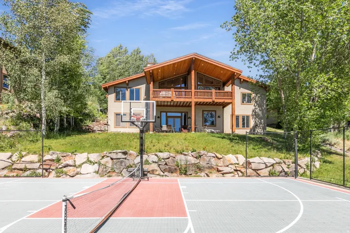 Multi-sport court featuring a basketball hoop and net, bordered by a stone retaining wall and lush greenery