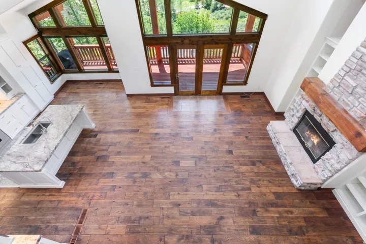 Spacious room with wood-finish flooring, a stone-faced fireplace with a natural wood mantel, and expansive windows
