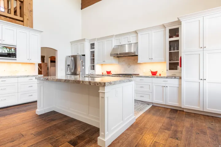 Gourmet kitchen featuring a large central island, white shaker-style cabinetry, stainless steel appliances, and wood-finish flooring