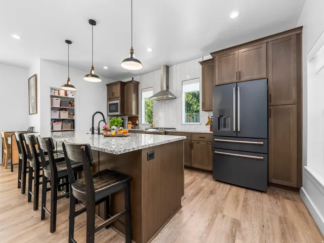 Open-concept kitchen featuring a large island with granite countertops, wood-finish flooring, and dark wood cabinetry