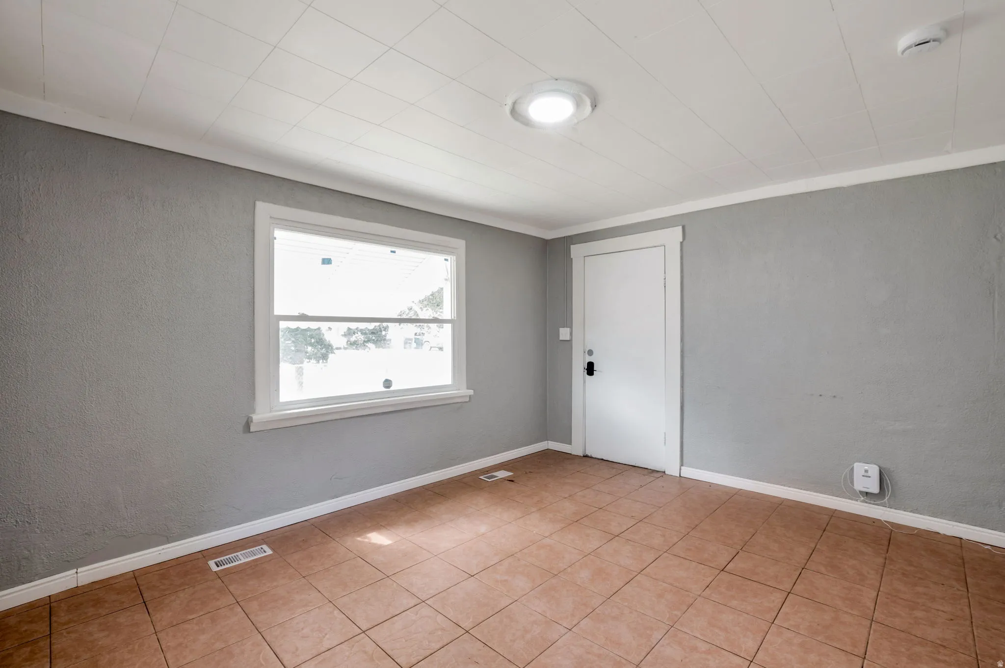 Neutral gray walls with white trim throughout, featuring a single window and a white panel door