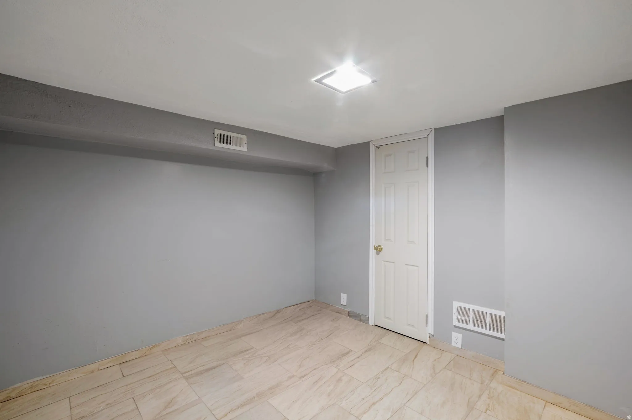 Room featuring light gray walls, tile flooring, a white paneled door, a ceiling-mounted light fixture, and floor-level vents