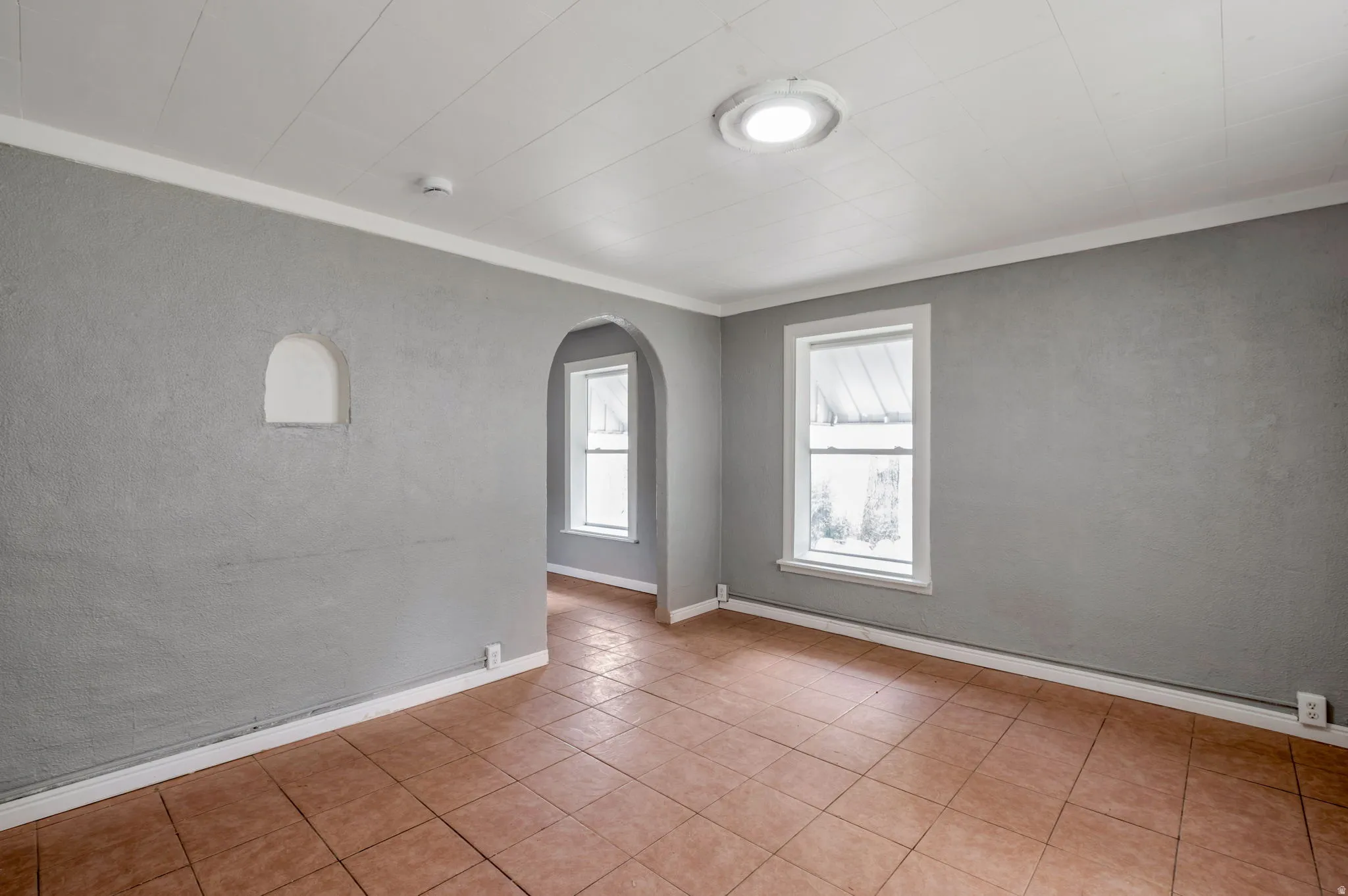 Room featuring terracotta-style tile flooring, textured gray walls, and white trim