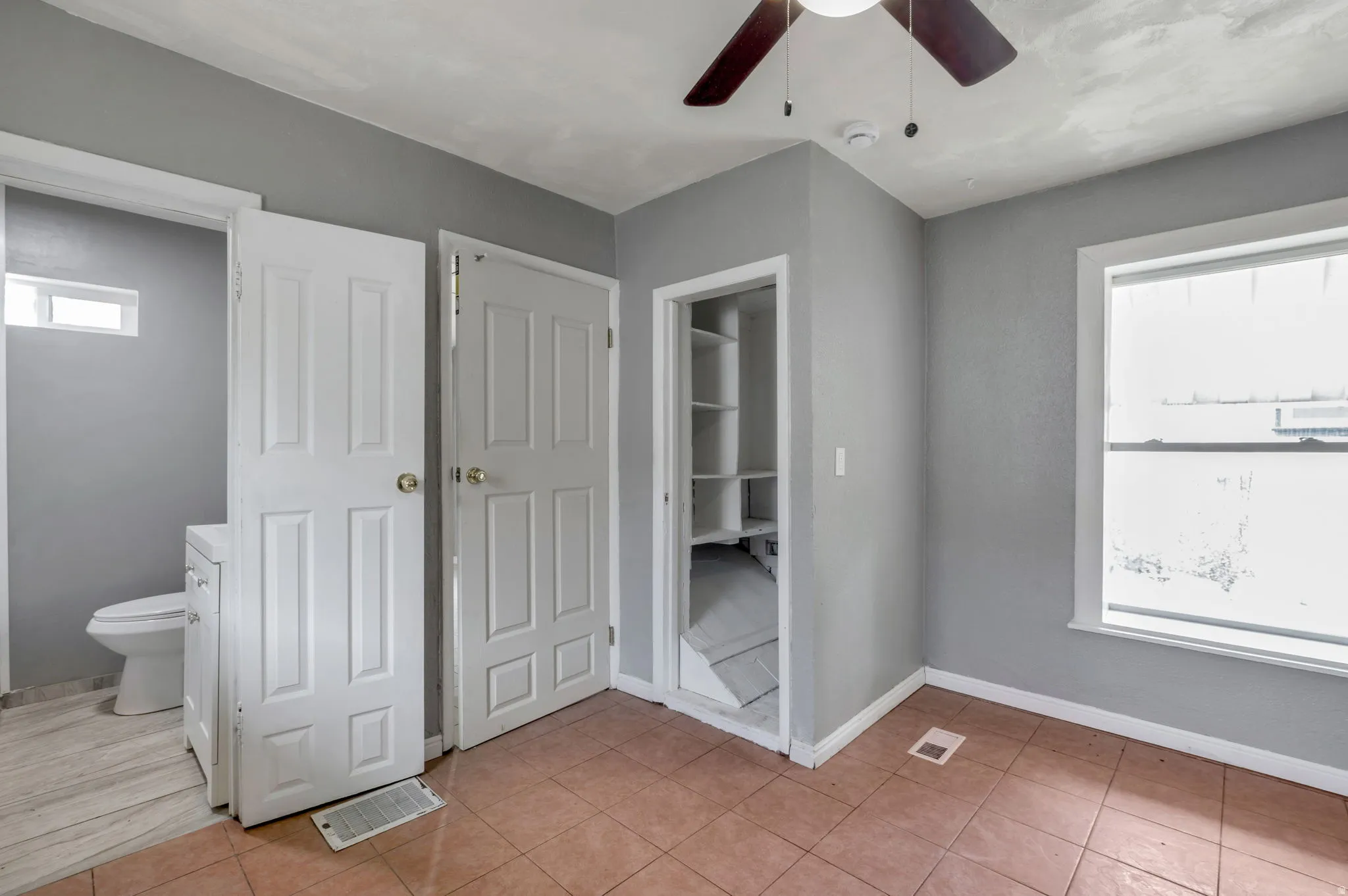 Room featuring neutral gray walls, tiled flooring, a ceiling fan, and a built-in shelving unit