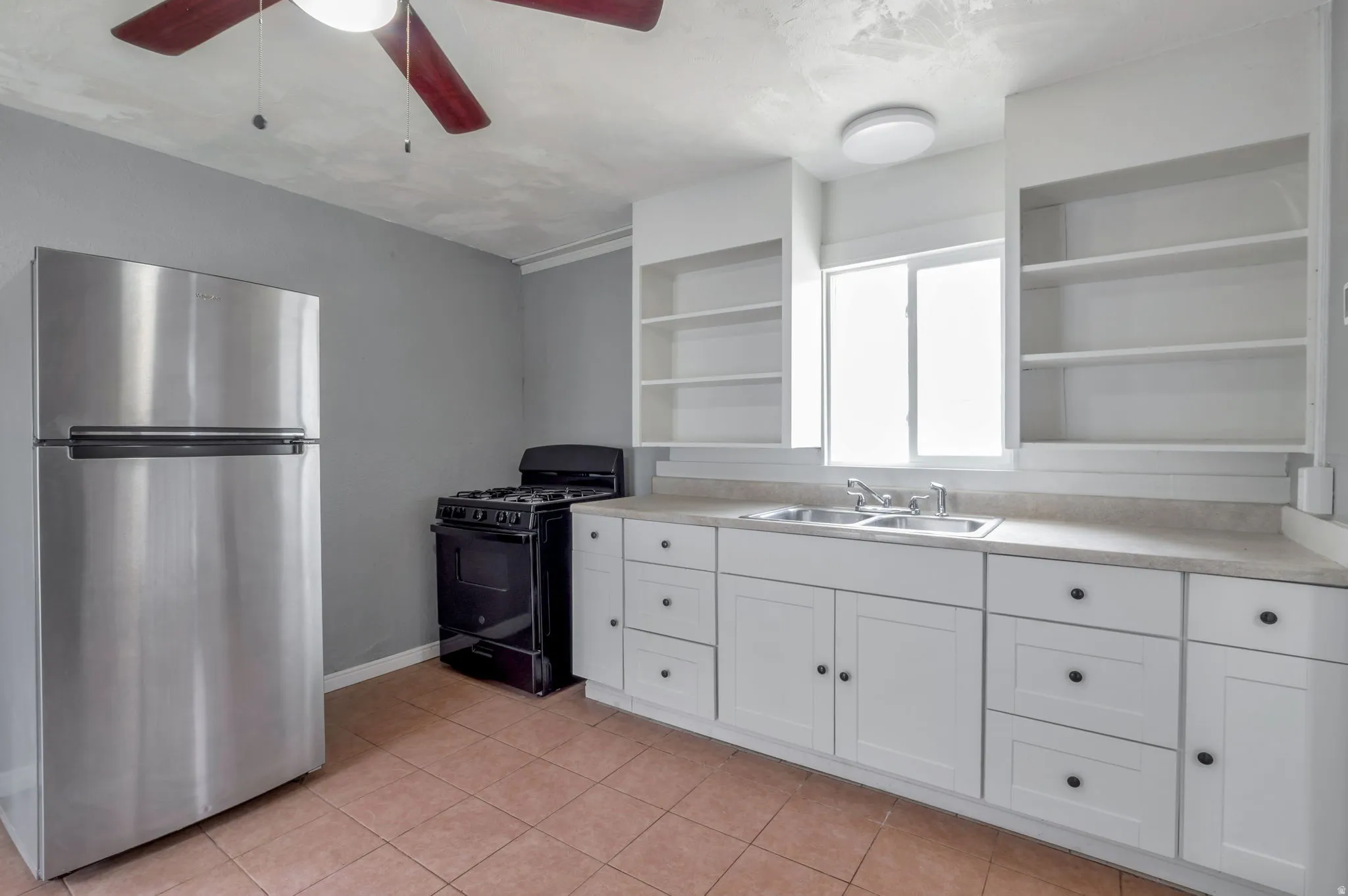Kitchen featuring a stainless steel refrigerator, black gas range, and white cabinetry