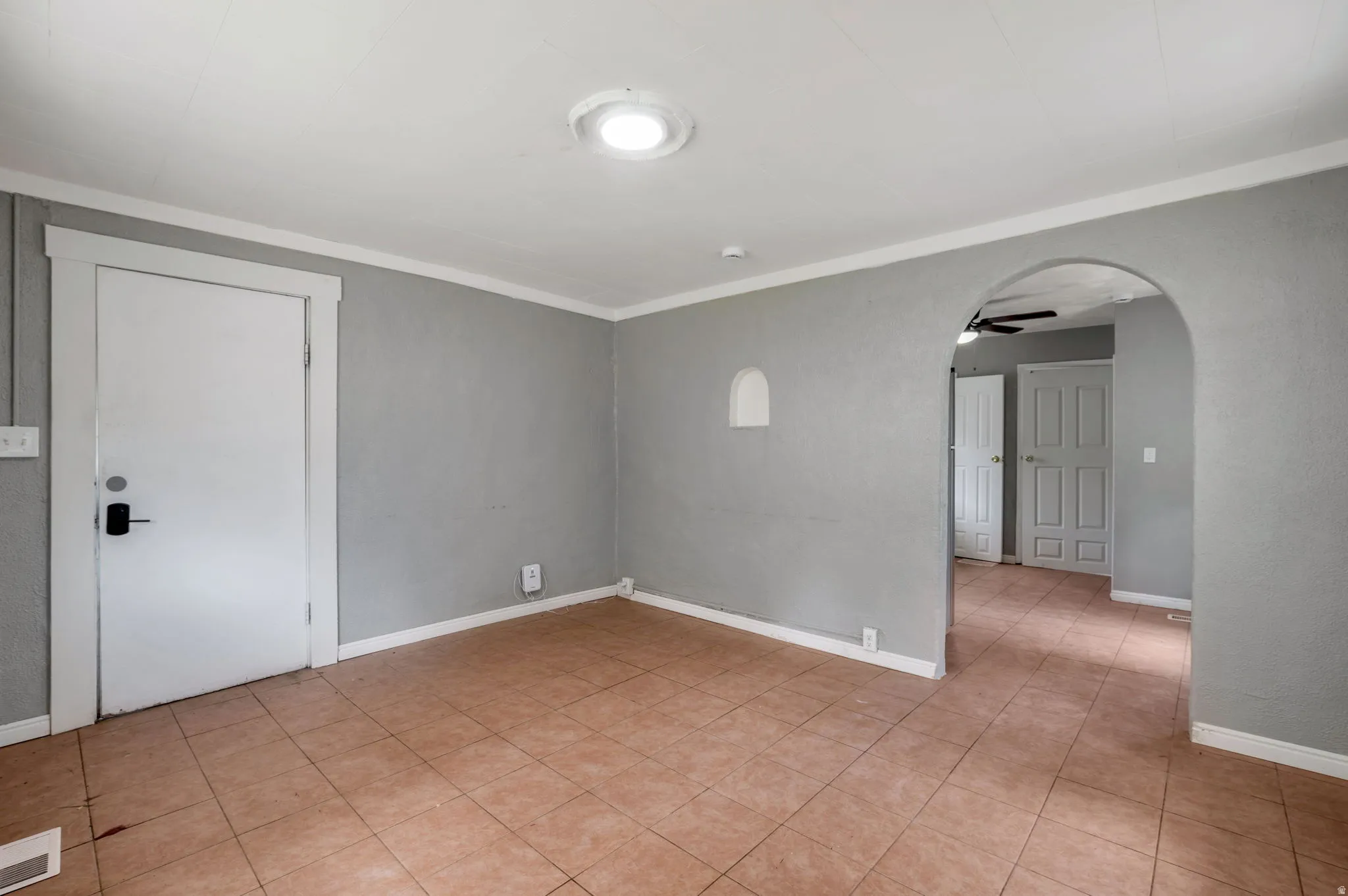 Room featuring light gray walls, white trim, terracotta-style floor tiling, an arched doorway, and a ceiling-mounted light fixture