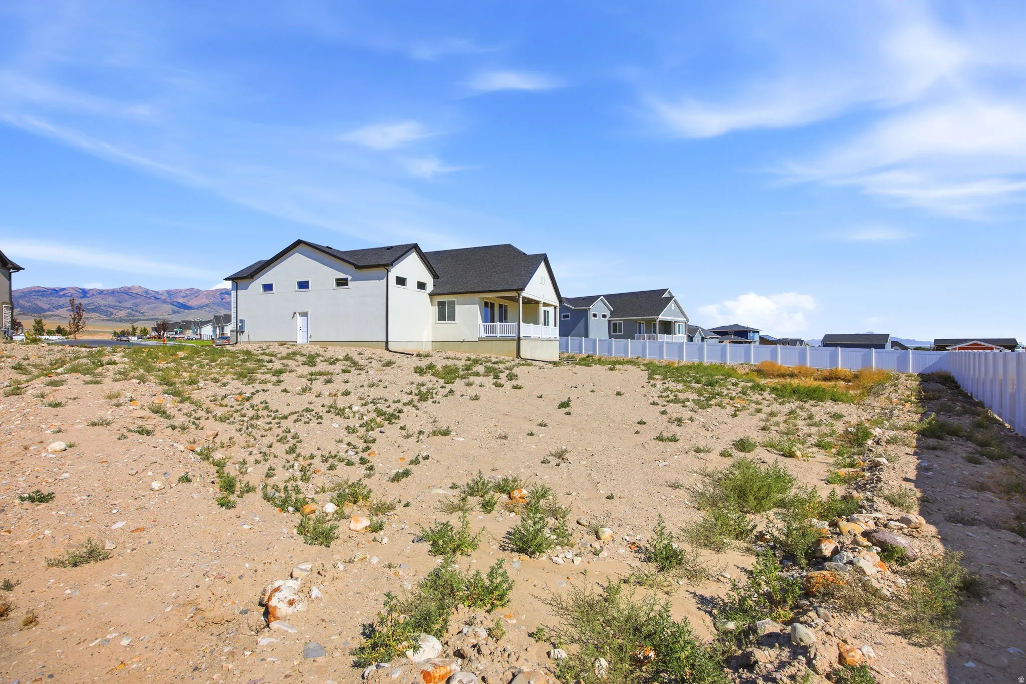 Level building site with a white vinyl privacy fence and mountain backdrop