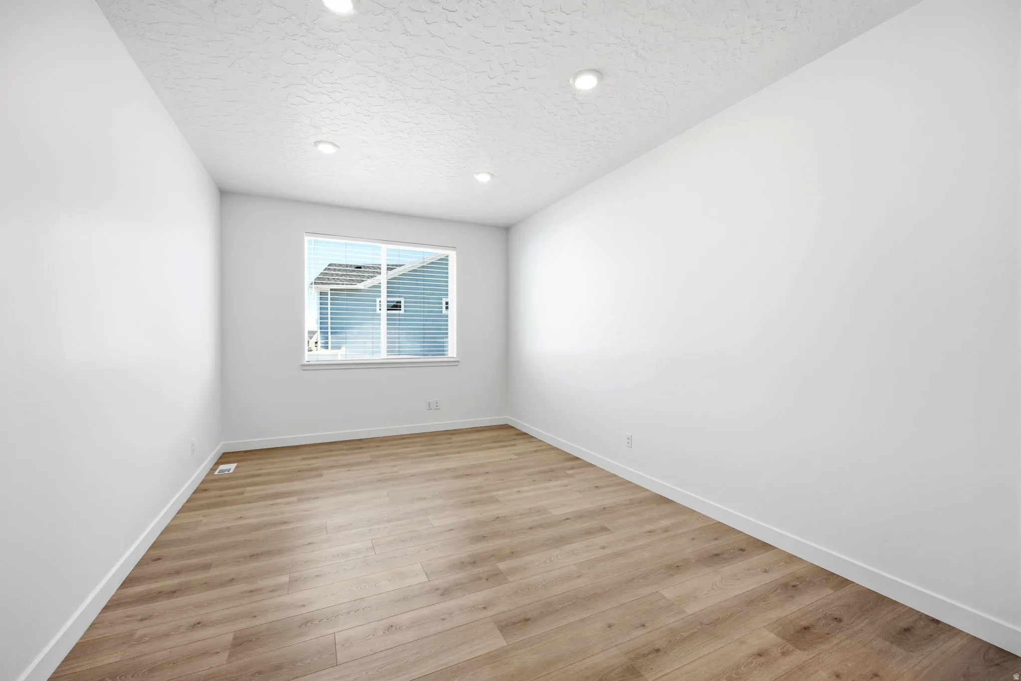 Spacious room featuring light wood-finish flooring, recessed lighting, a large window, white walls, and white baseboards