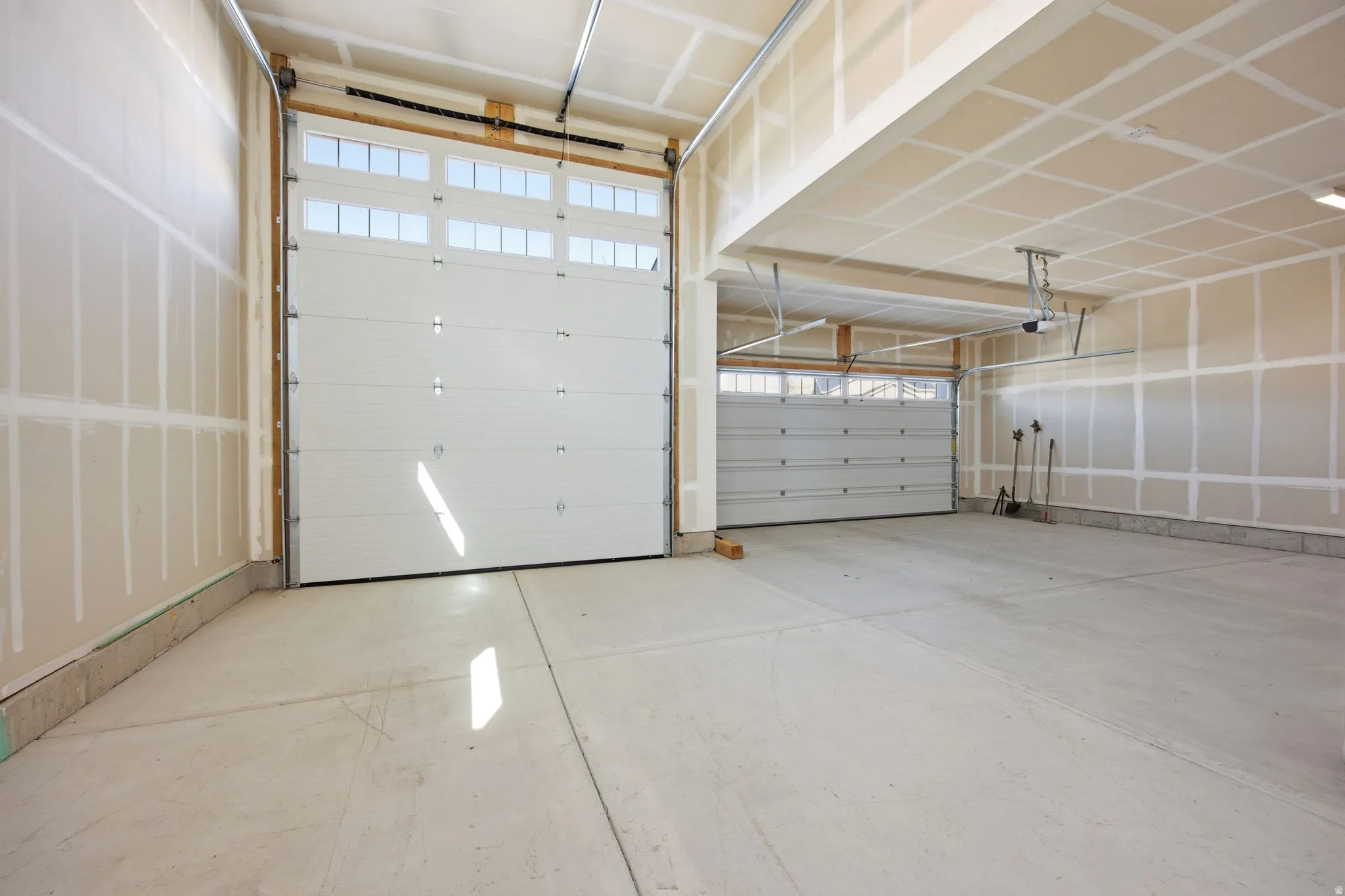Three-car garage featuring concrete flooring, a large white garage door with upper window panels, a second garage door, and unfinished interior walls
