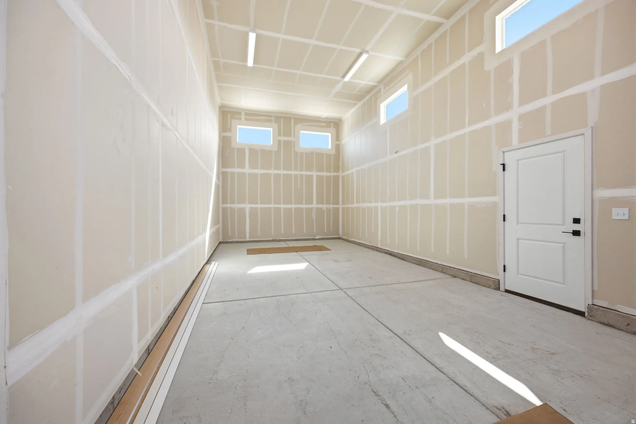 RV garage featuring a concrete floor, unpainted drywall, high ceilings, multiple upper transom windows, and a white interior door with black hardware