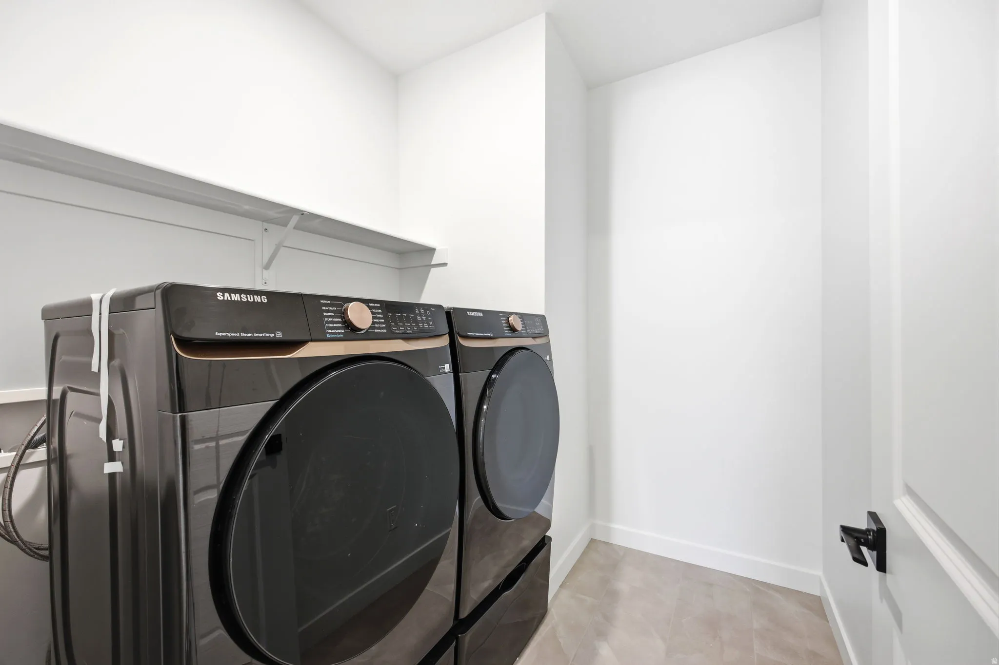 Dedicated laundry area featuring a wall-mounted shelf, light-toned flooring, and neutral wall finishes