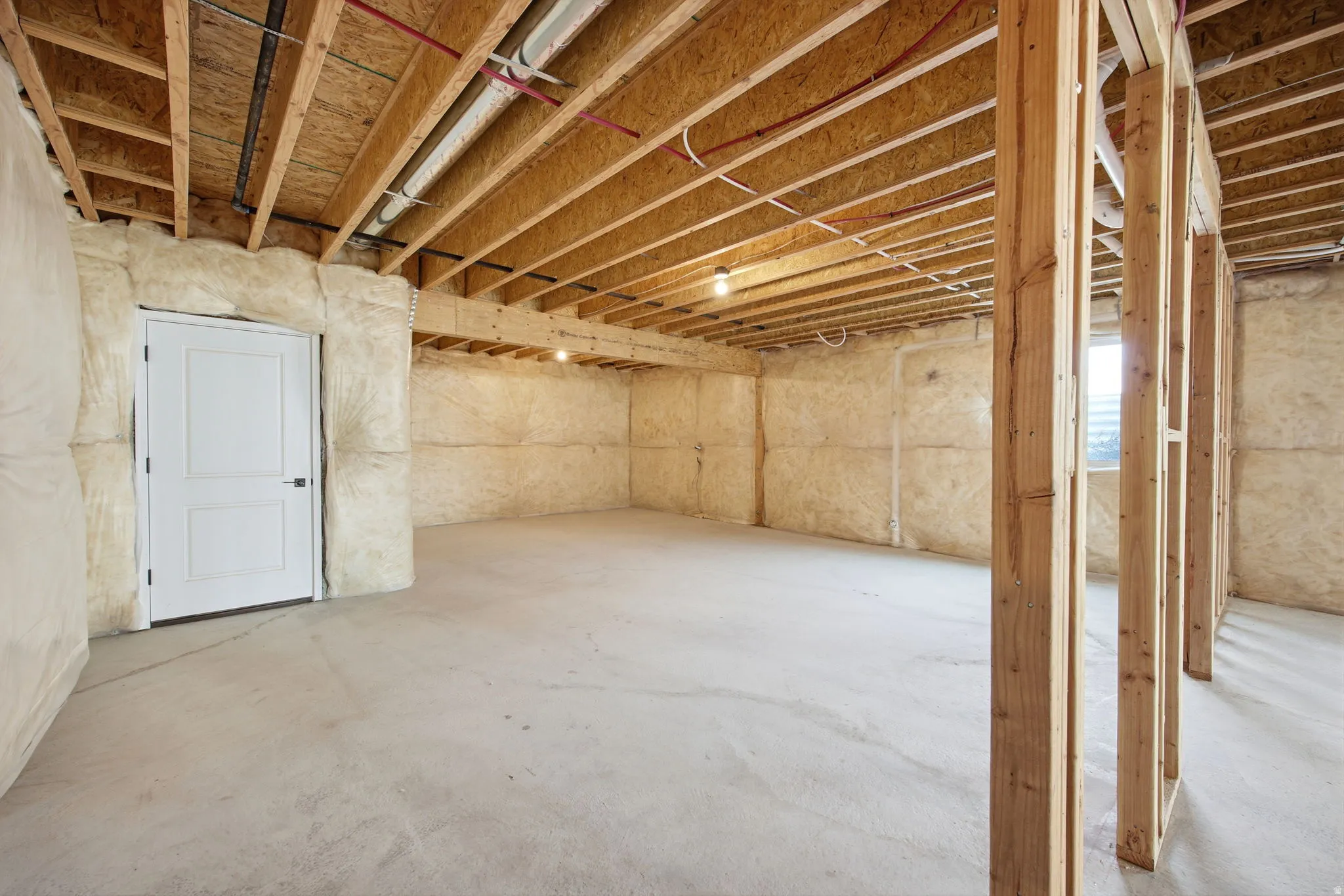 Spacious unfinished basement offering exposed ceiling joists, insulated exterior walls, concrete flooring, and a framed interior partition