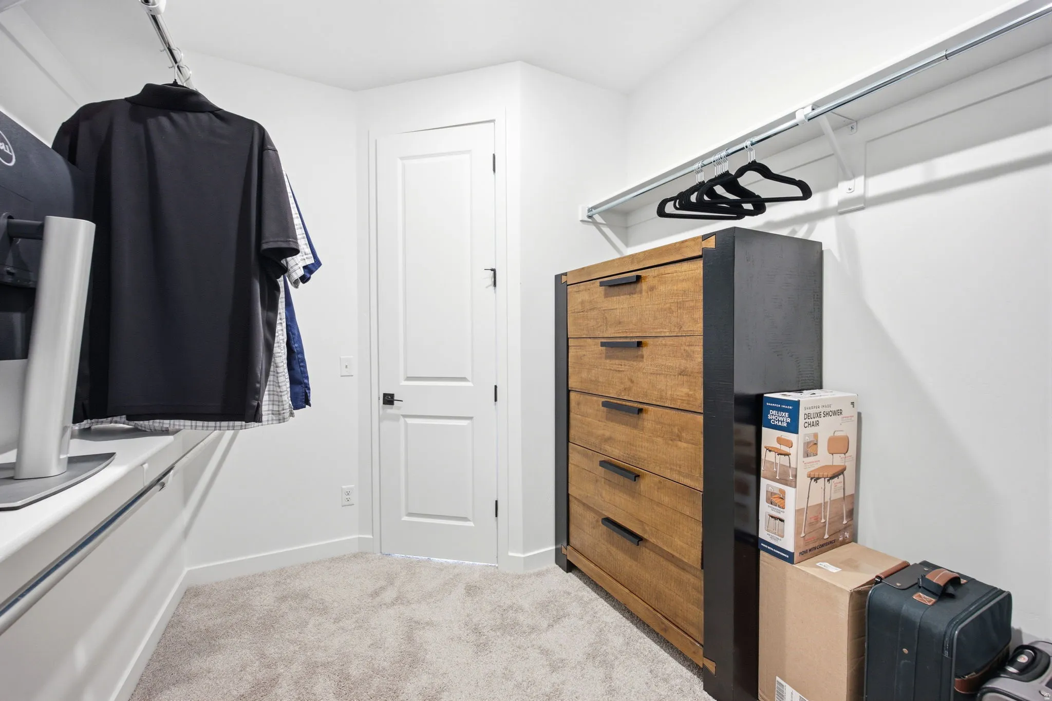 Walk-in closet featuring light-colored carpet flooring, white walls, and a white door with black hardware