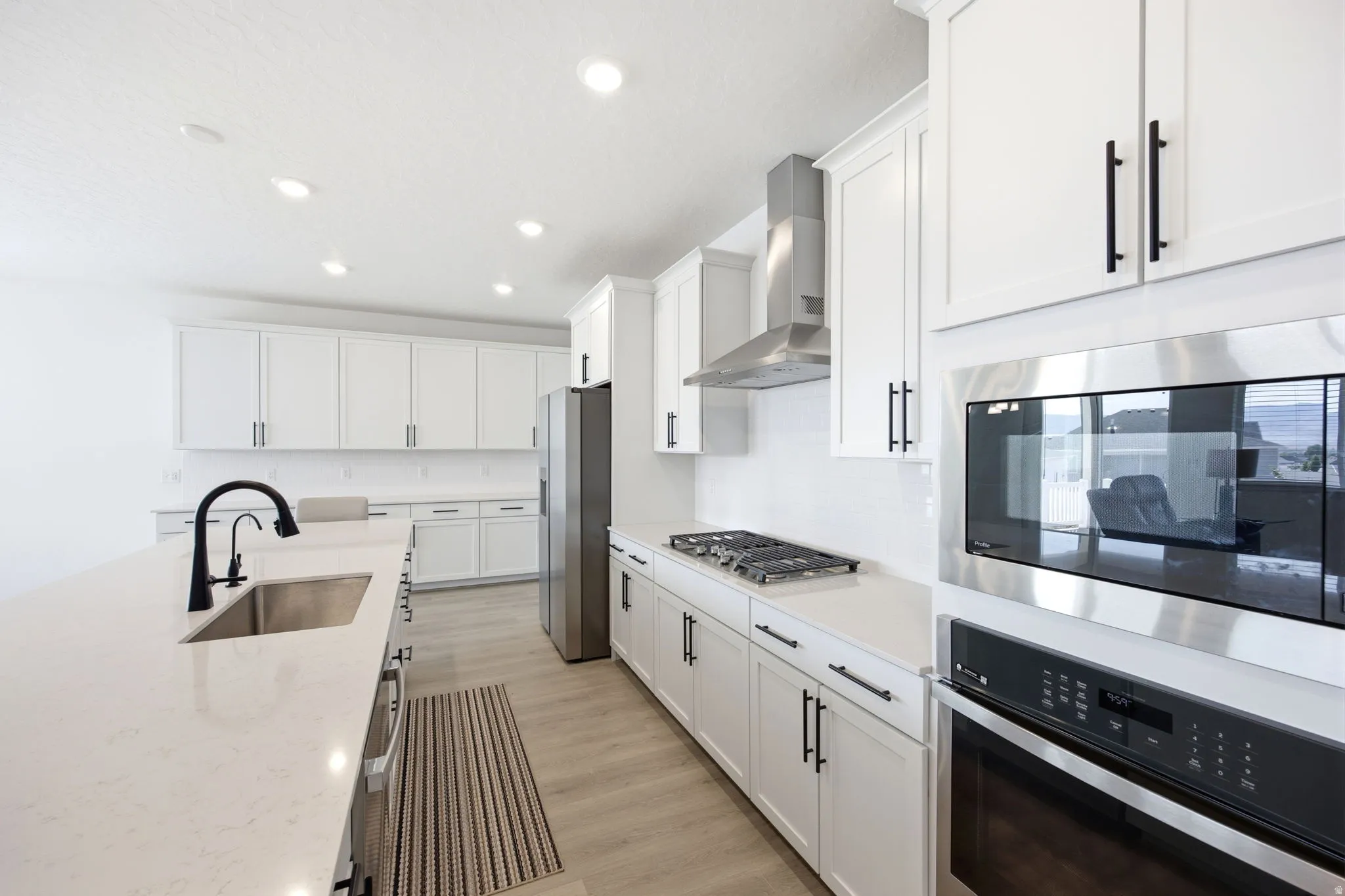 Modern kitchen featuring white cabinetry, light-toned countertops, stainless steel appliances, a large island with an undermount sink, and wood-finish flooring