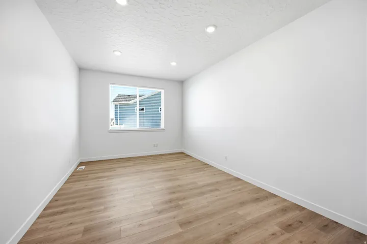 Spacious room featuring light wood-finish flooring, recessed lighting, a large window, white walls, and white baseboards